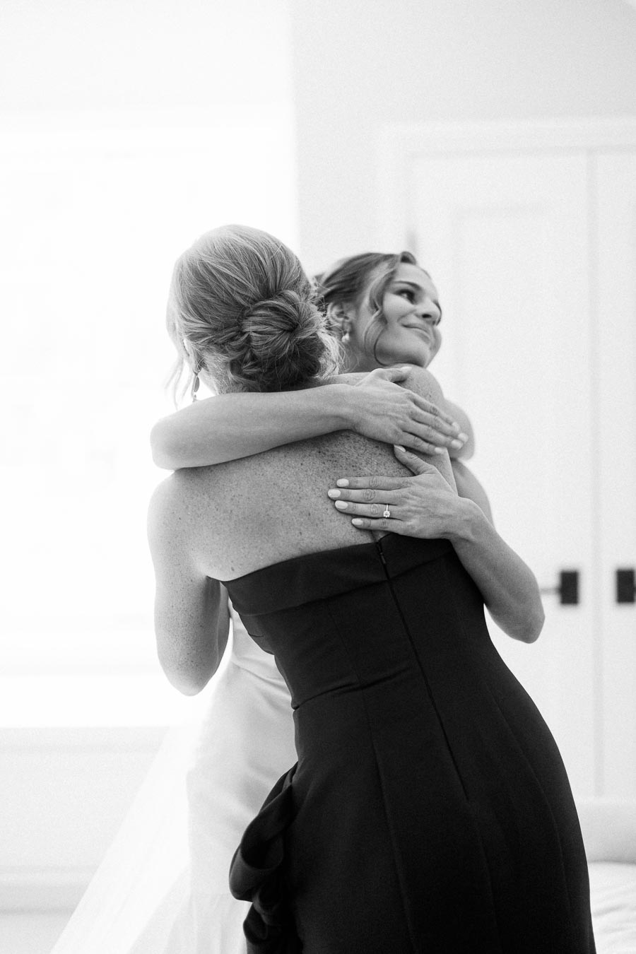 Black and white photo of a bride hugging a woman during wedding morning preparations indoors near Chatham-Kent, Ontario.