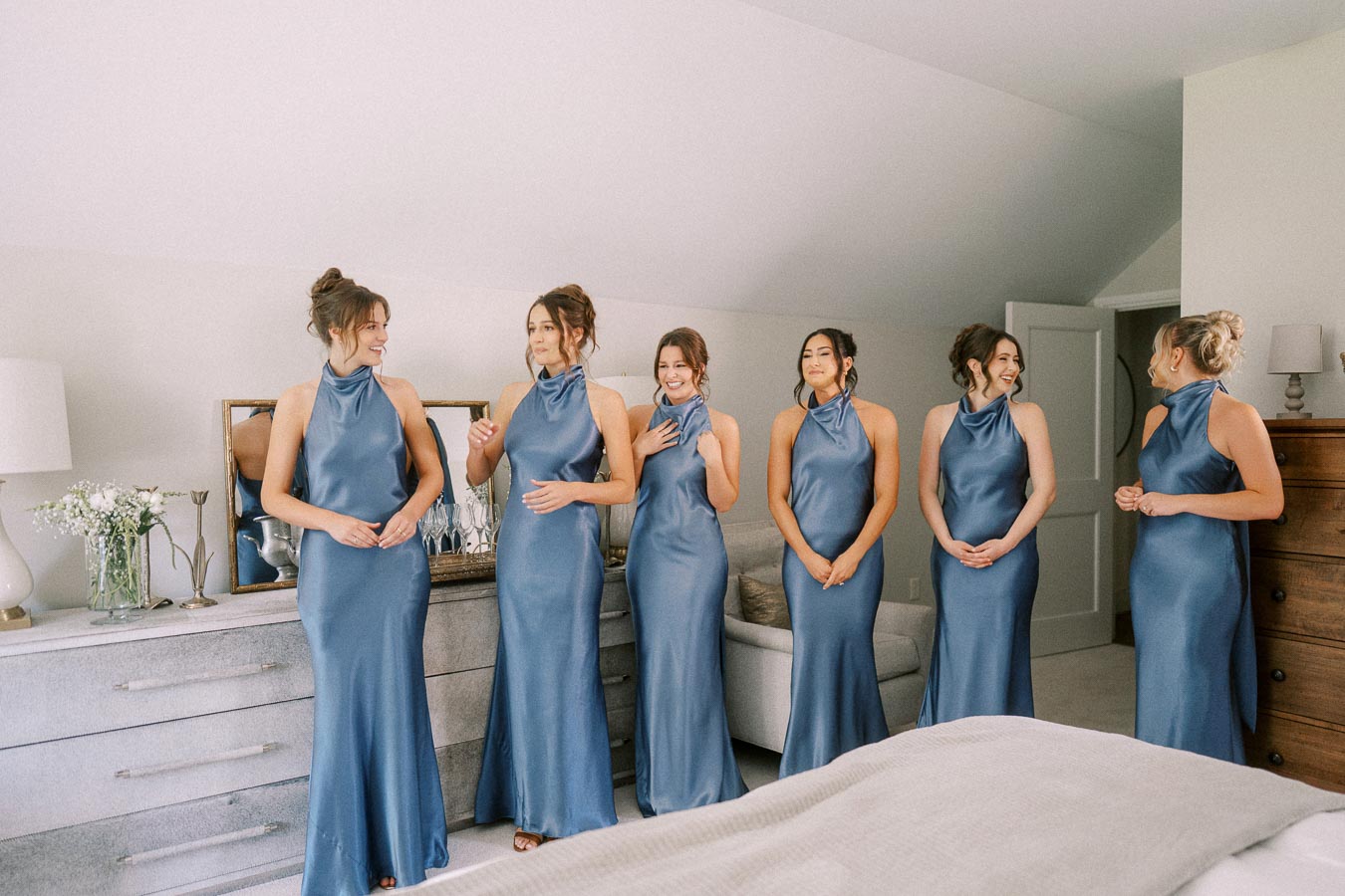 Six bridesmaids in matching blue satin dresses stand together in a bright bedroom during a wedding morning near Chatham-Kent, Ontario.