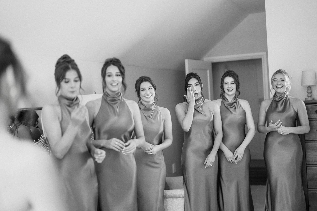 Black and white photo of bridesmaids in matching satin dresses smiling indoors during a wedding morning near Chatham-Kent, Ontario.