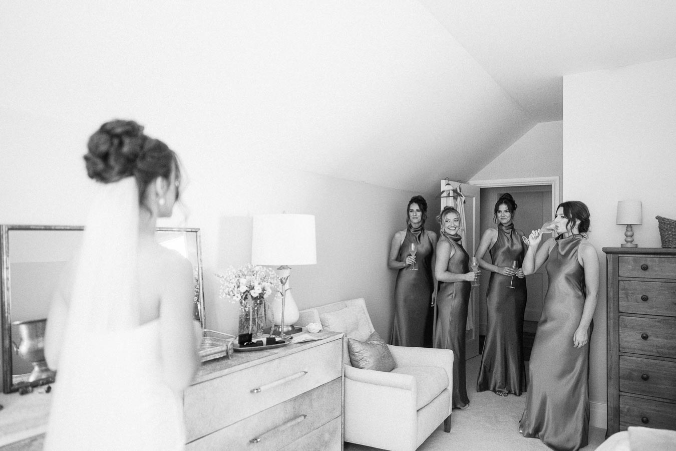 Black and white photo of a bride in a veil facing four bridesmaids in long dresses inside a bedroom near Chatham-Kent, Ontario.