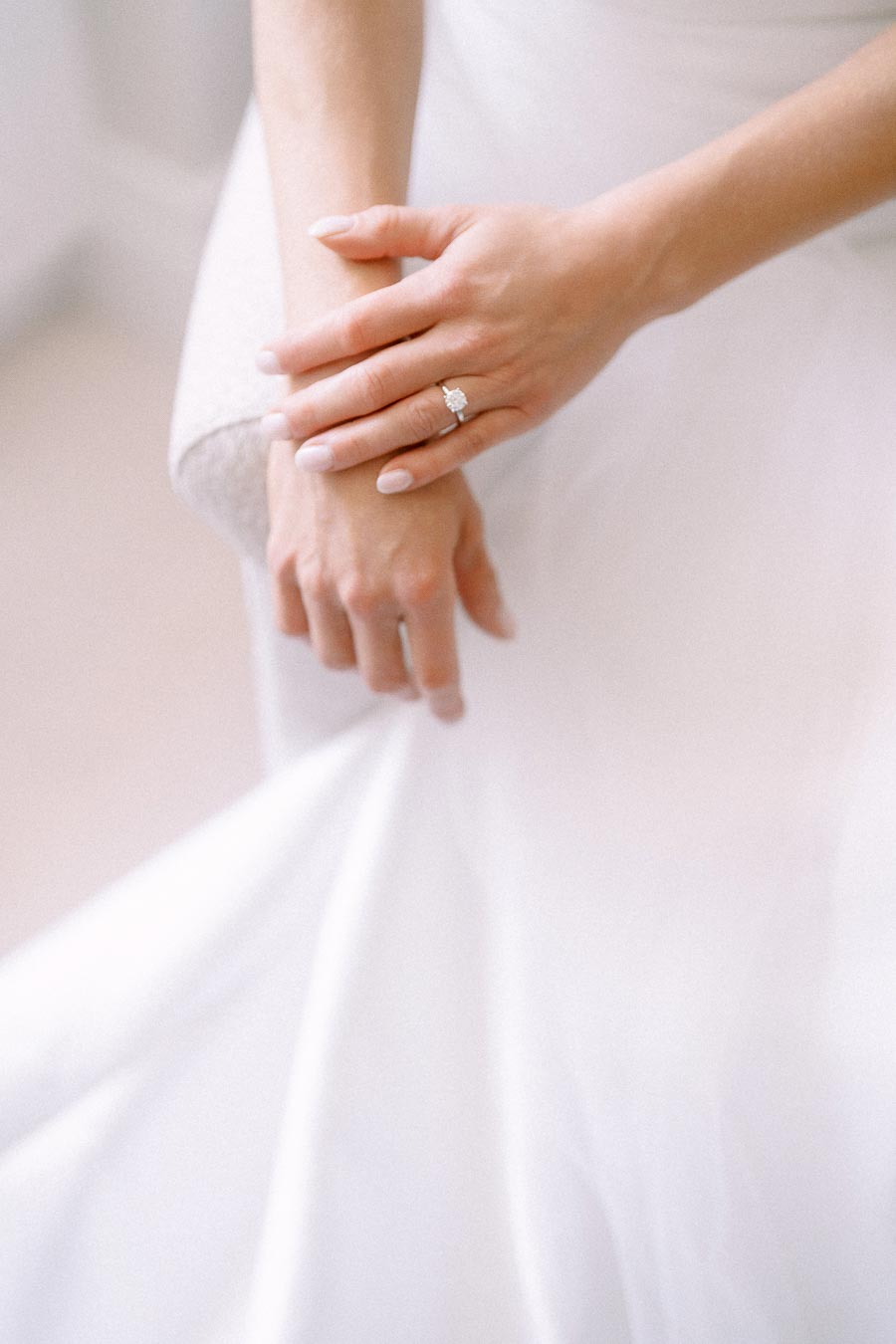 Close up of a bride wearing a diamond engagement ring and white wedding dress, holding her wrist during a soft bridal morning portrait in Ontario.