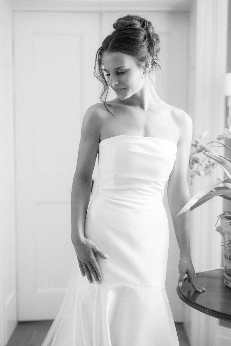 Black and white portrait of a bride in a strapless wedding dress standing by a window in Chatham-Kent, Ontario.