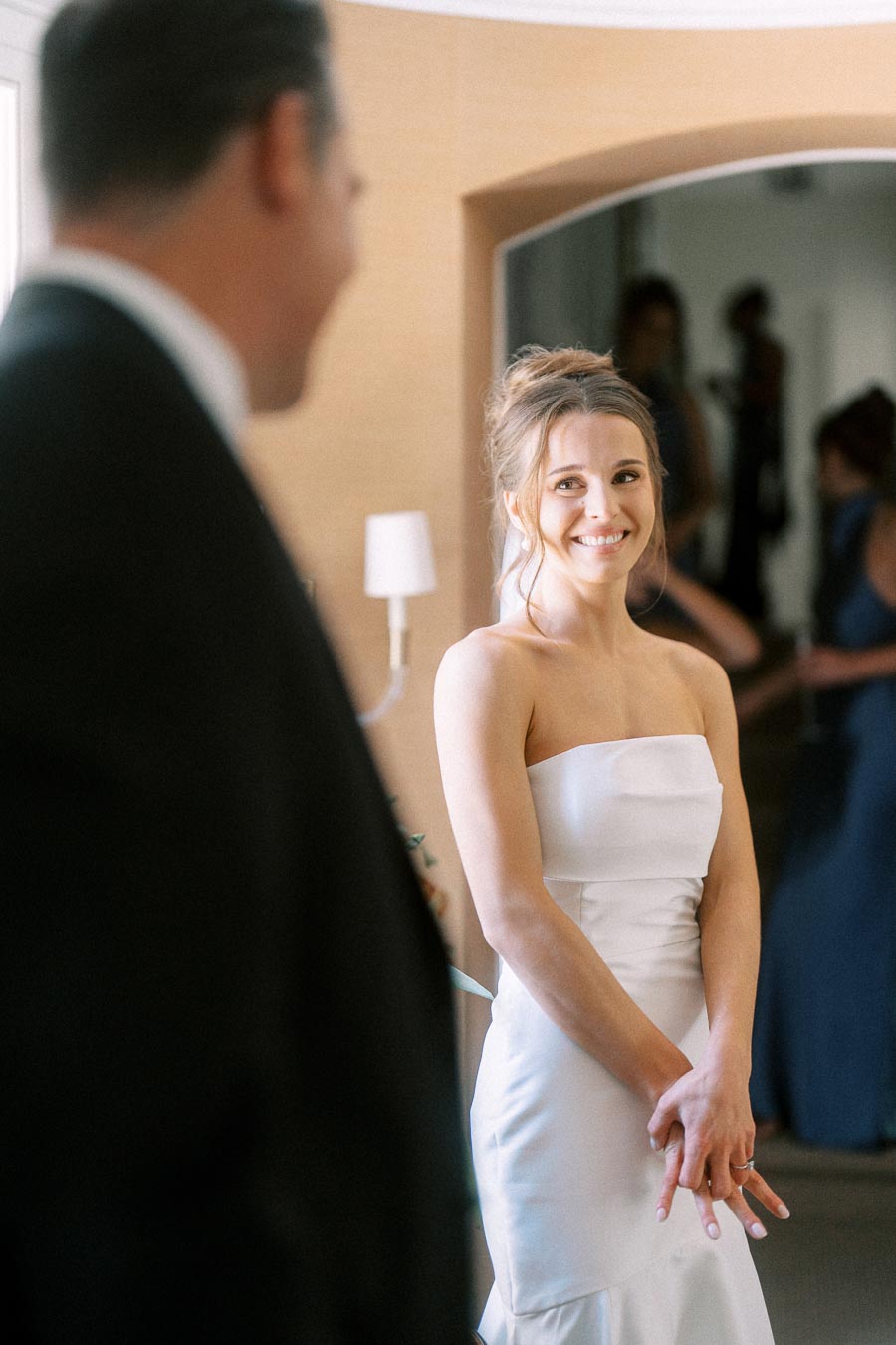 Bride in a white strapless wedding dress smiles at her father during a first look indoors near Chatham-Kent, Ontario.