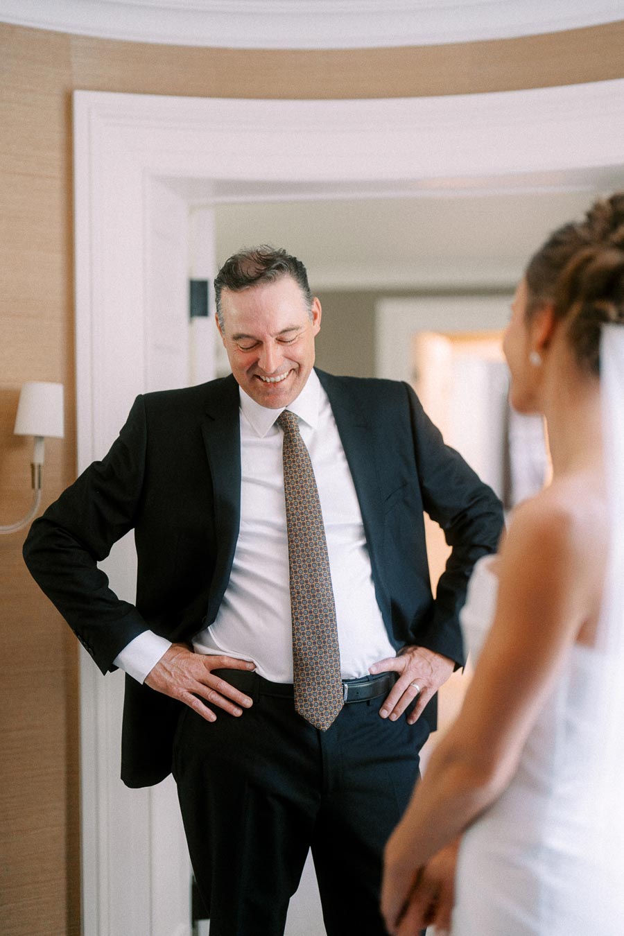 Smiling father in a black suit sees his daughter in a white wedding dress during a private estate wedding morning near Chatham-Kent, Ontario.