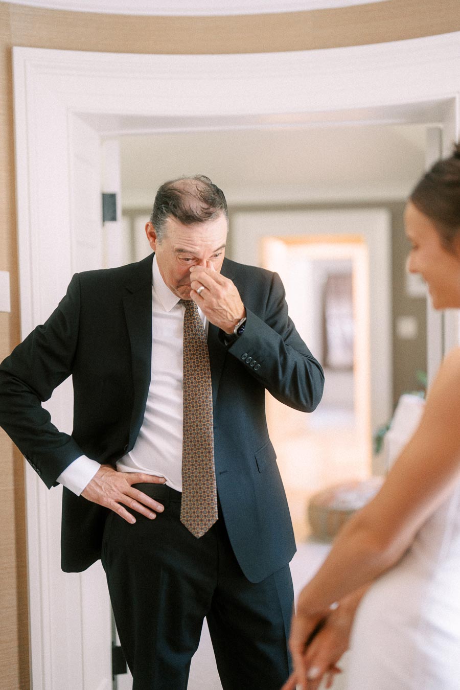 Emotional father in a black suit wipes tears during first look with bride in white wedding dress inside a home near Chatham-Kent, Ontario.