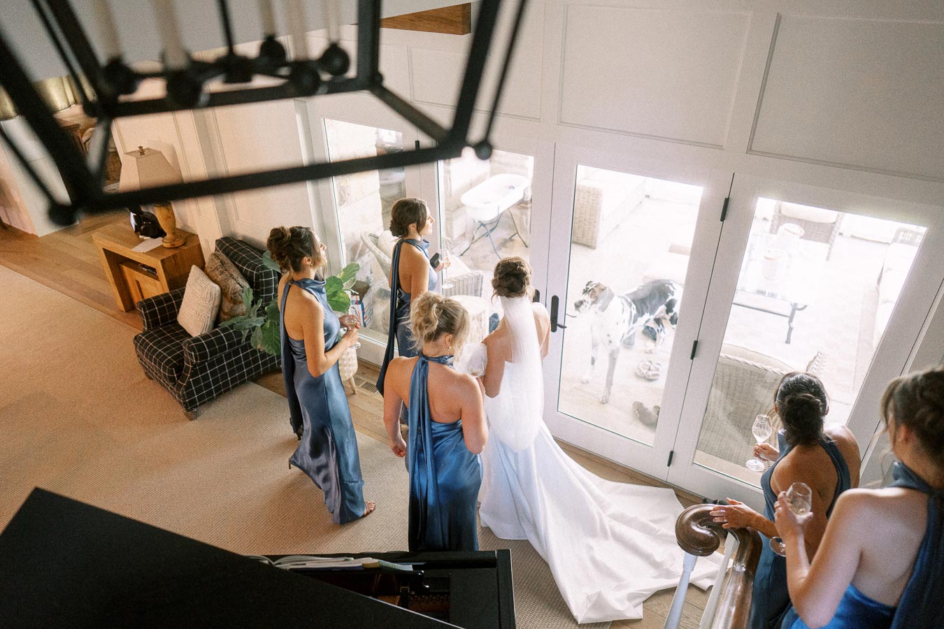 Bride in white gown with bridesmaids in blue dresses gathered by glass doors during a private estate wedding in Chatham-Kent, Ontario.