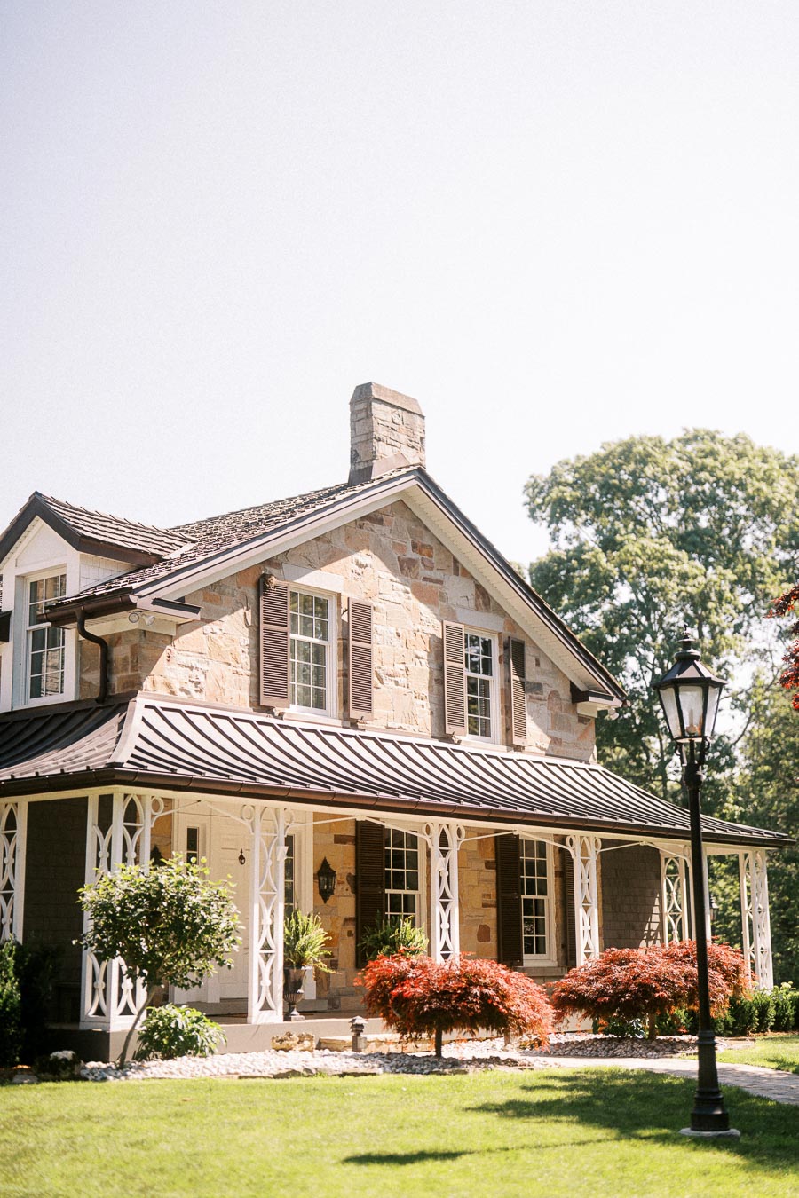 Stone private estate house with wraparound porch, shutters, landscaped garden, lawn, and lamppost near Chatham-Kent, Ontario.