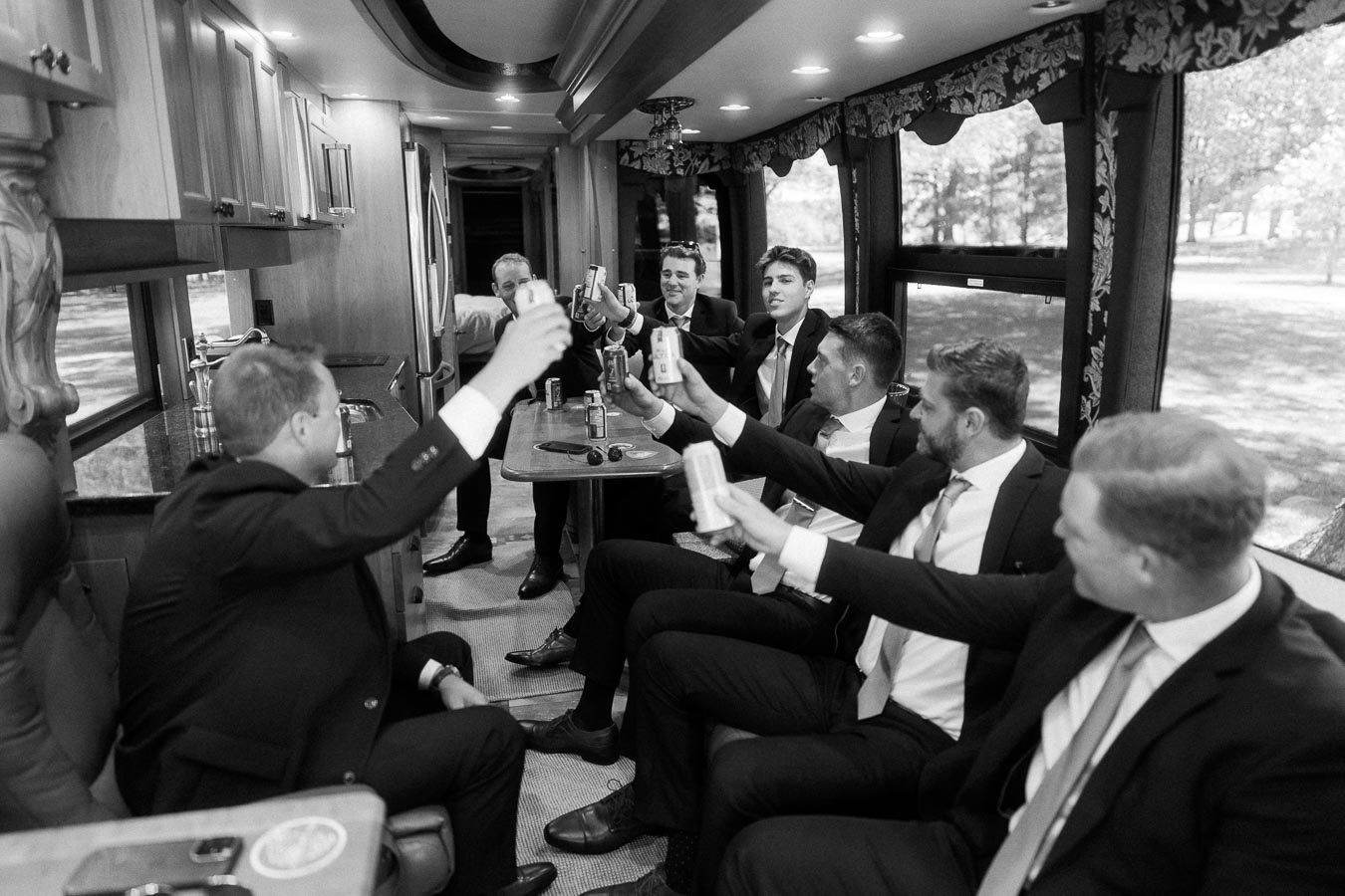 Groomsmen in suits toast with cans inside a motorhome near Chatham-Kent, Ontario, before an outdoor private estate wedding.