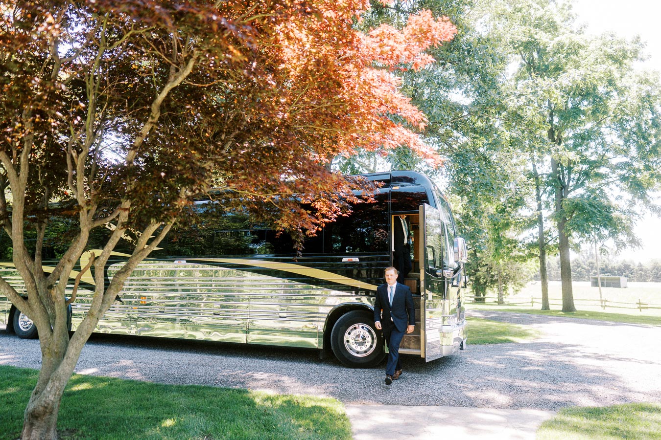 Groom in a navy suit steps from a black motorcoach on a tree lined private estate driveway near Chatham Kent, Ontario.