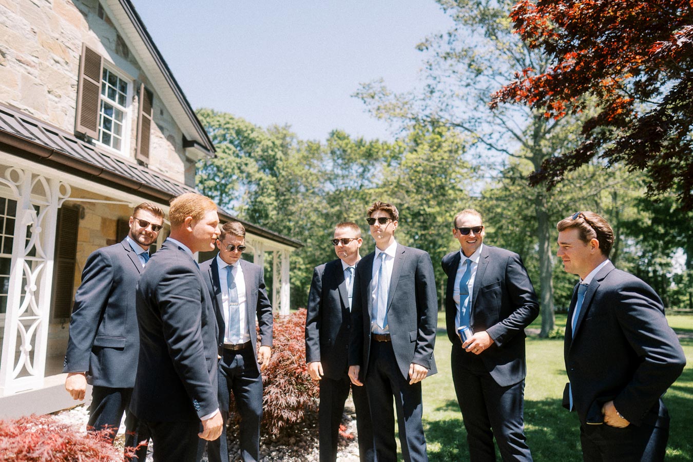 Groom and groomsmen in dark suits standing outside a stone private estate in Chatham-Kent, Ontario, during an outdoor wedding first look.