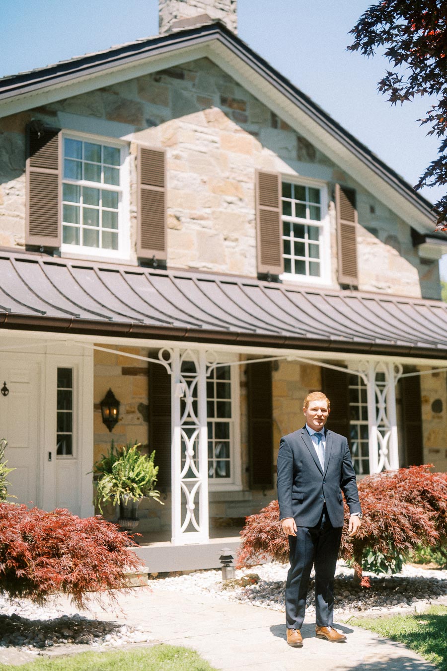 Groom in a dark suit standing outside a stone estate house in Chatham-Kent, Ontario, before a wedding first look.