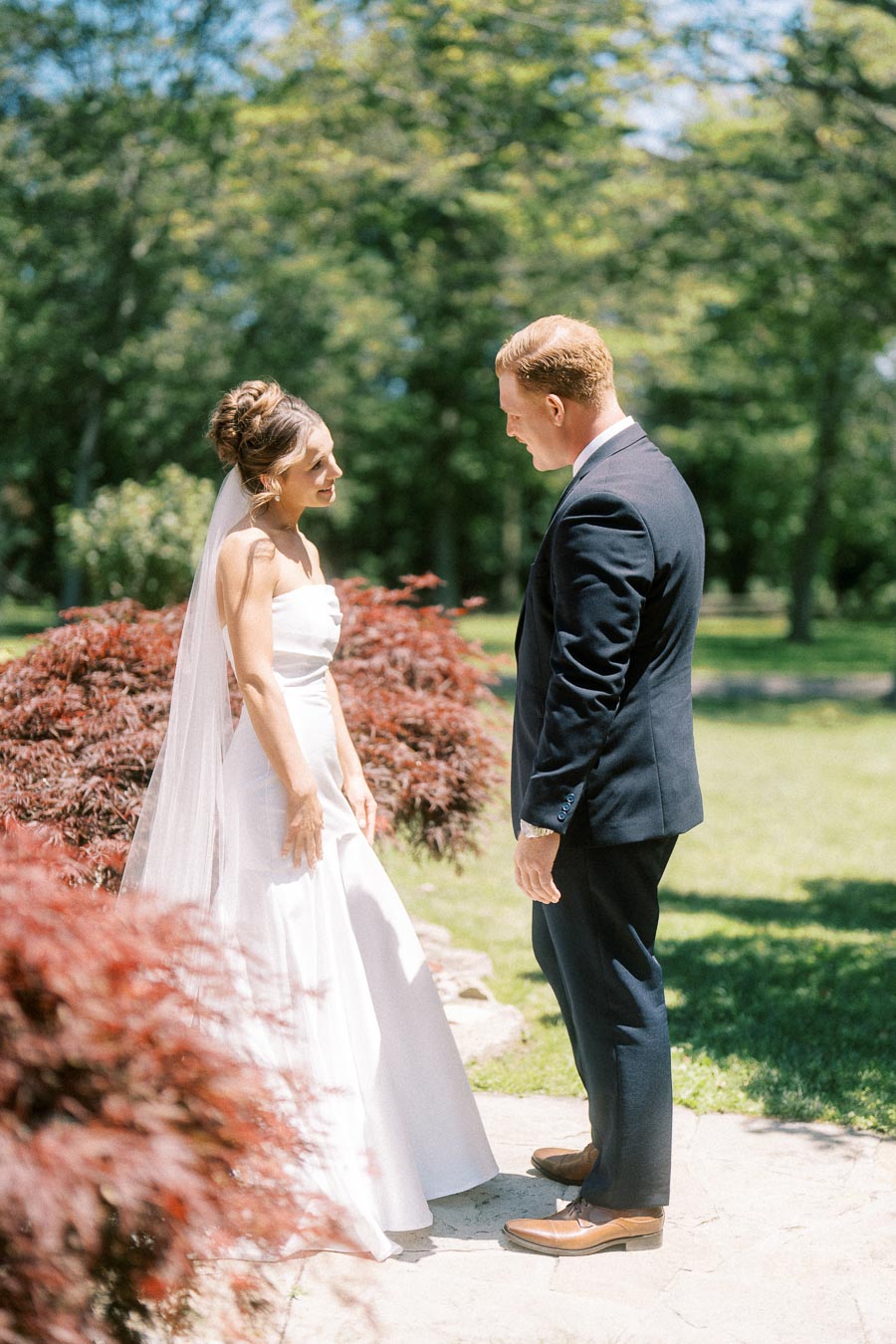 Bride and groom share a first look outdoors on a private estate near Chatham-Kent, Ontario, with trees, lawn, and red shrubs.