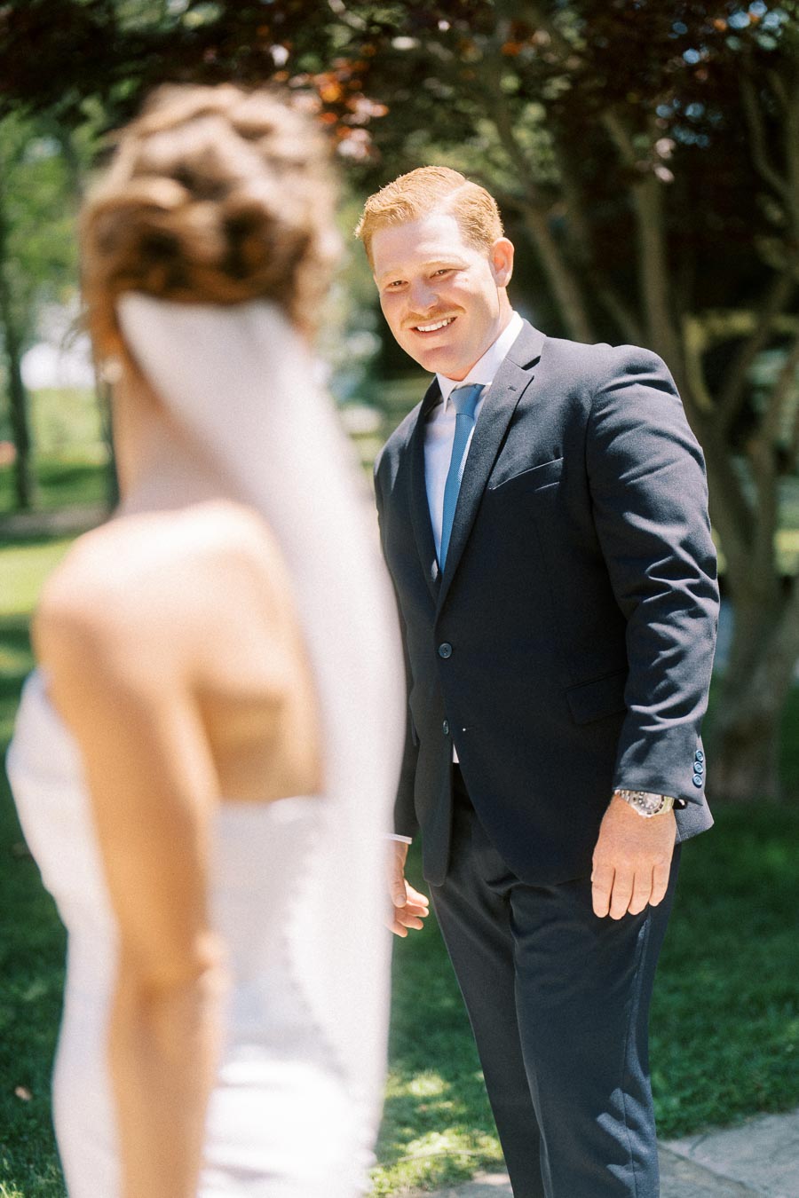 Groom smiling at bride during first look outdoors on a sunny private estate near Chatham-Kent, Ontario, Canada.