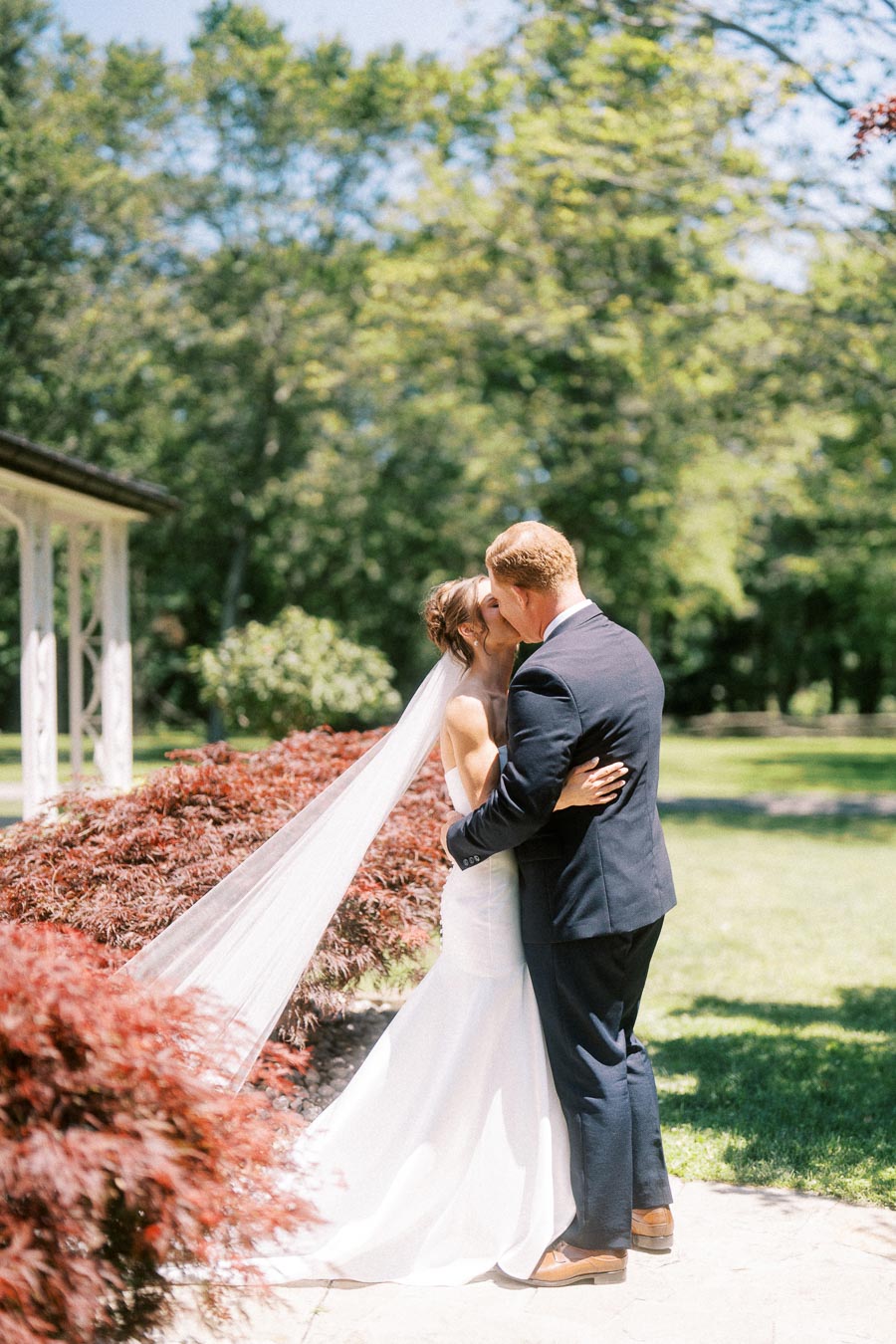Bride and groom kiss during a first look in a sunny garden near Chatham-Kent, Ontario, Canada.