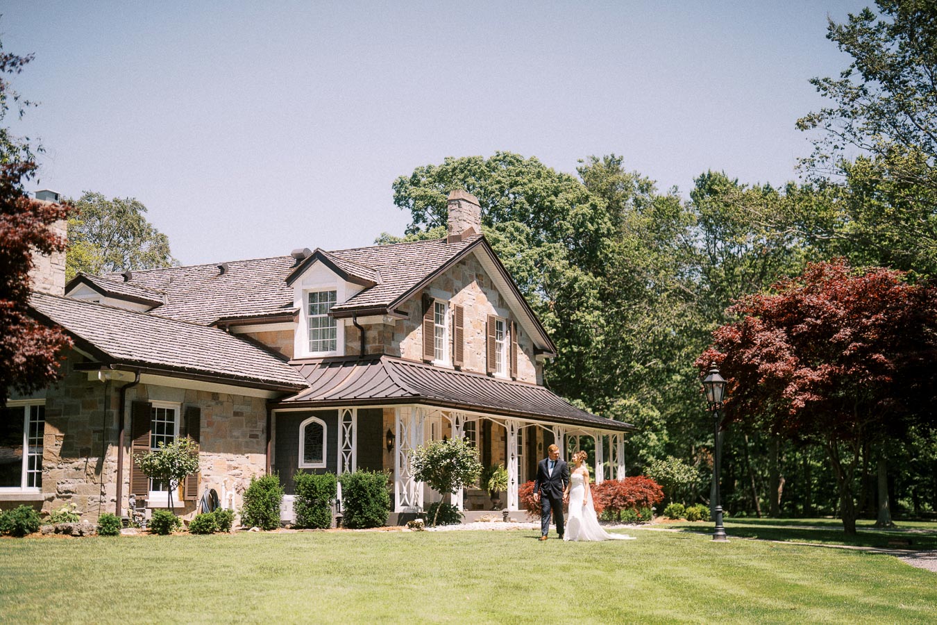 Bride and groom walking on a lawn in front of a stone private estate house in Chatham-Kent, Ontario, Canada.