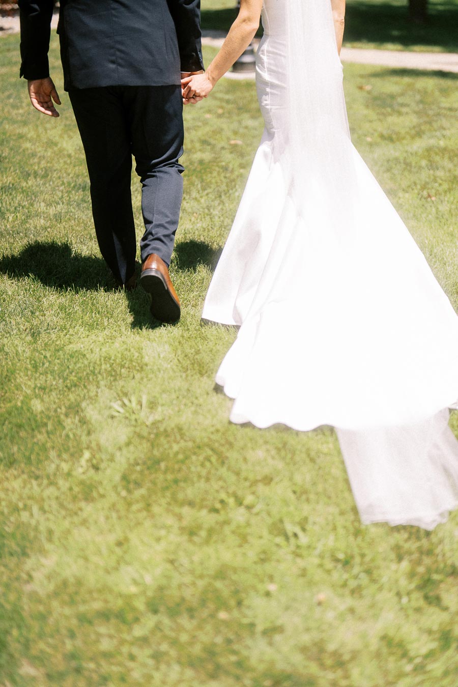 Bride and groom holding hands while walking across a sunny grass lawn during an outdoor wedding near Chatham-Kent, Ontario, Canada.