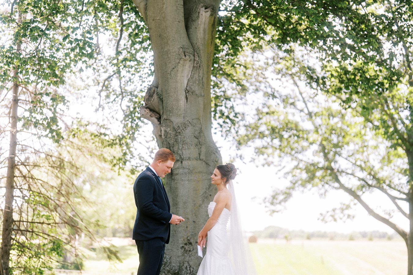 Bride and groom reading private vows under a large tree at an outdoor estate wedding near Chatham-Kent, Ontario, Canada.