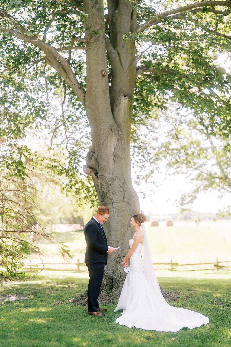 Bride and groom reading vows beneath a large tree at a private outdoor estate wedding near Chatham-Kent, Ontario, Canada.