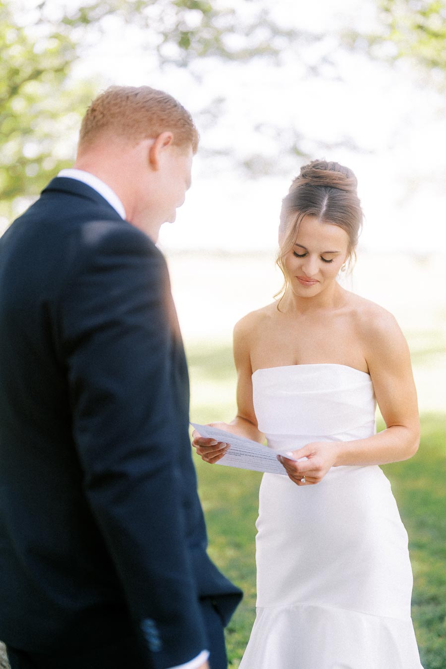 Bride and groom reading private wedding vows outdoors under a tree on a sunny estate lawn near Chatham-Kent, Ontario.