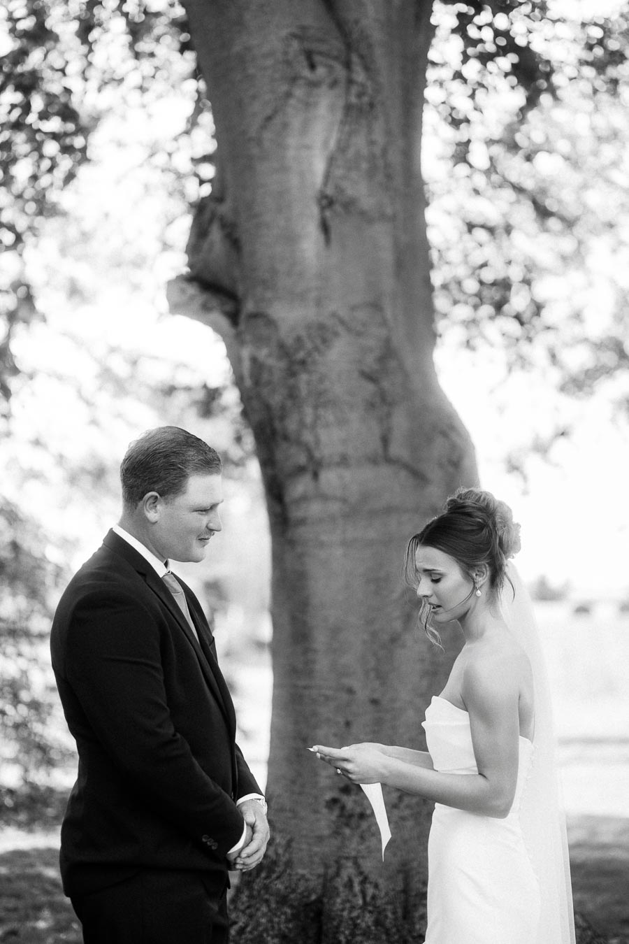 Black and white portrait of a bride reading vows to a groom under a large tree during a private outdoor wedding near Chatham-Kent, Ontario.