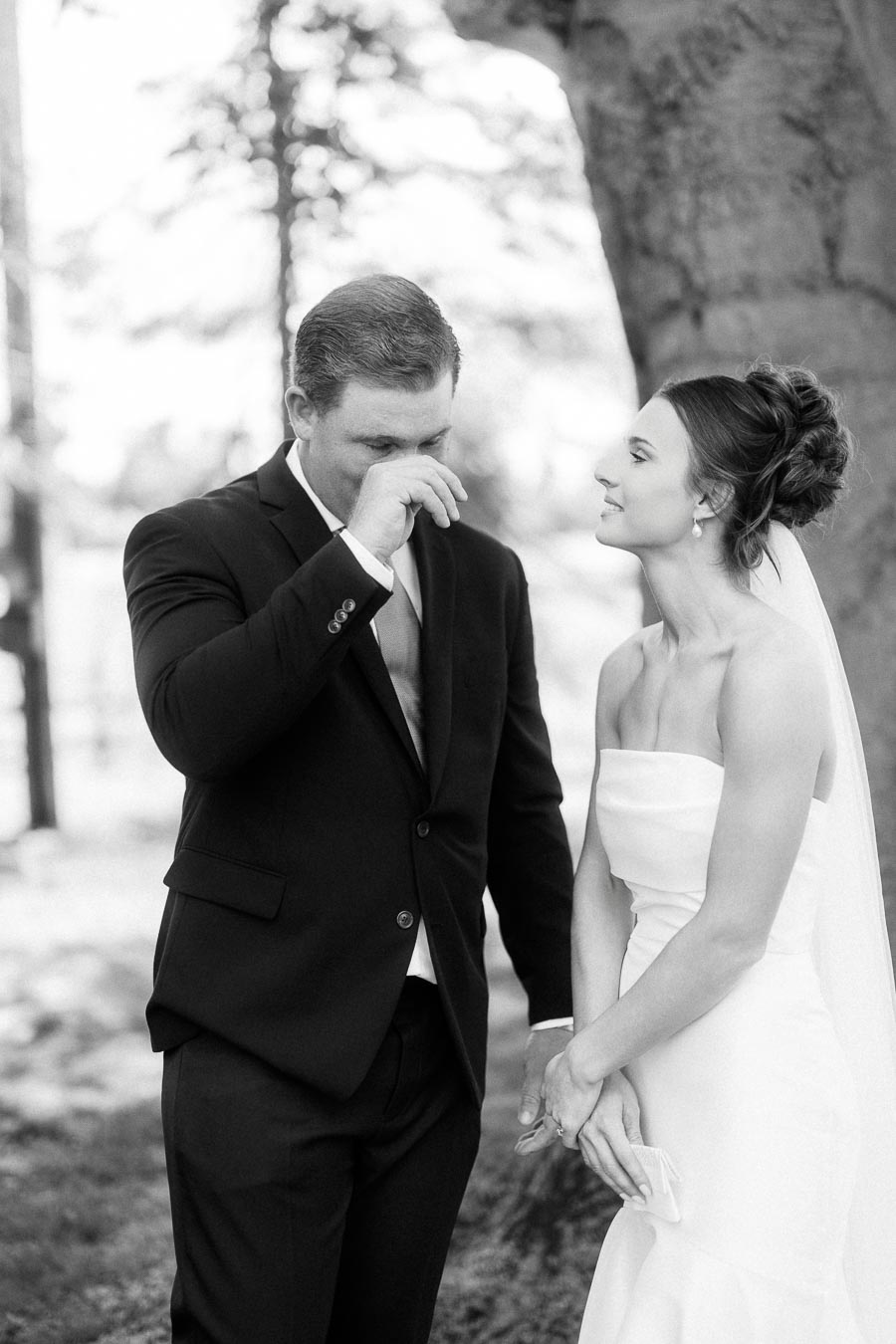 Black and white portrait of a bride and emotional groom holding hands under a tree during private wedding vows near Chatham-Kent, Ontario.
