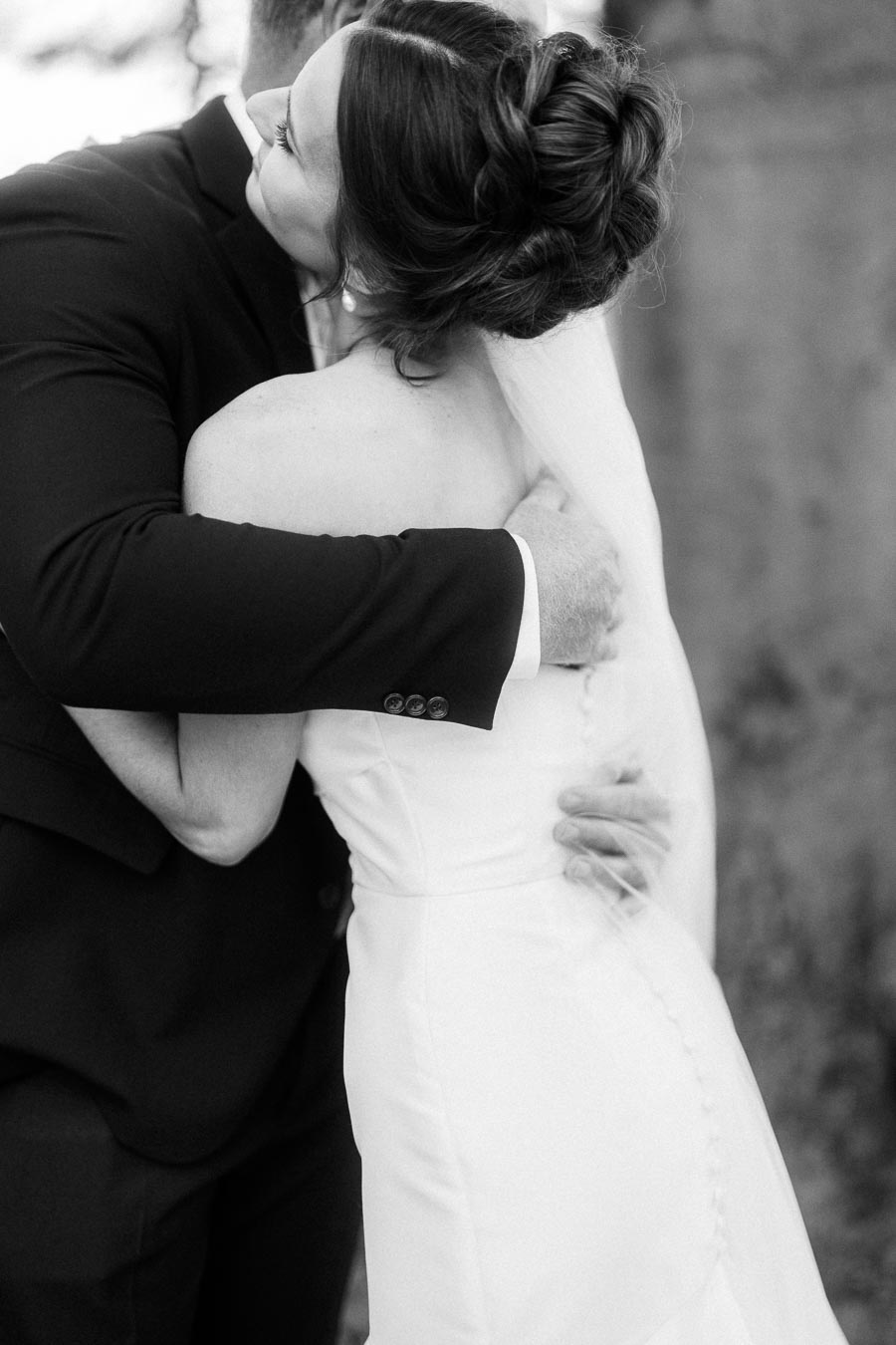 Black and white wedding portrait of groom embracing bride in strapless gown and veil outdoors near Chatham-Kent, Ontario.