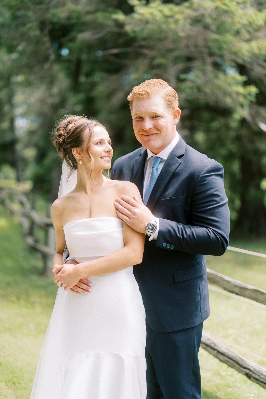 Bride and groom posing outdoors by a rustic fence on a farm estate near Chatham Kent, Ontario, Canada.