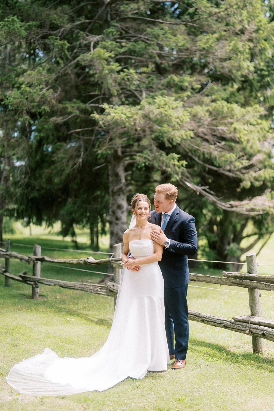 Bride and groom posing outdoors by a rustic wooden fence on a private farm estate near Chatham-Kent, Ontario, Canada.