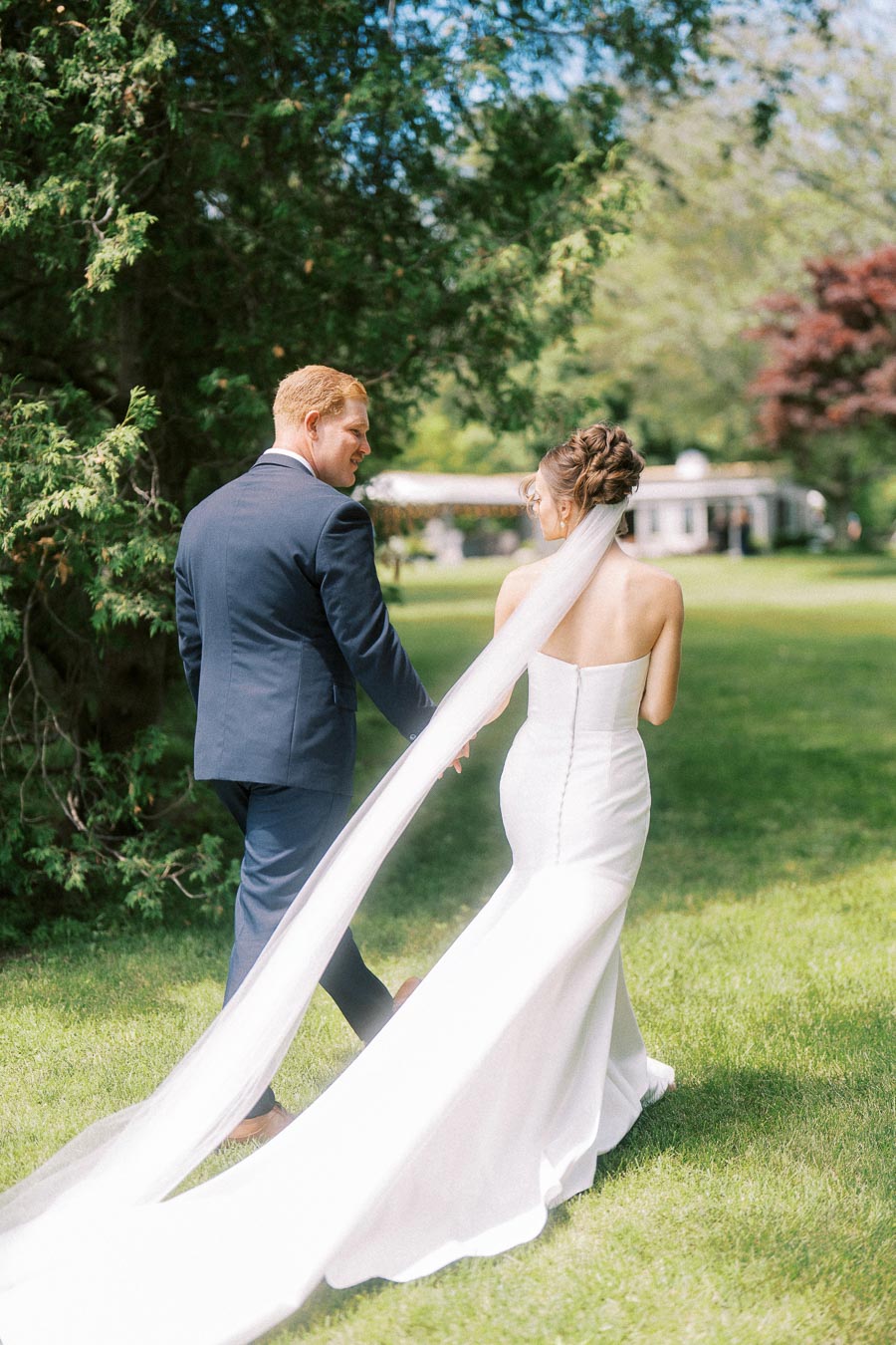 Bride and groom walking hand in hand across a sunny lawn during an outdoor private estate wedding near Chatham-Kent, Ontario.