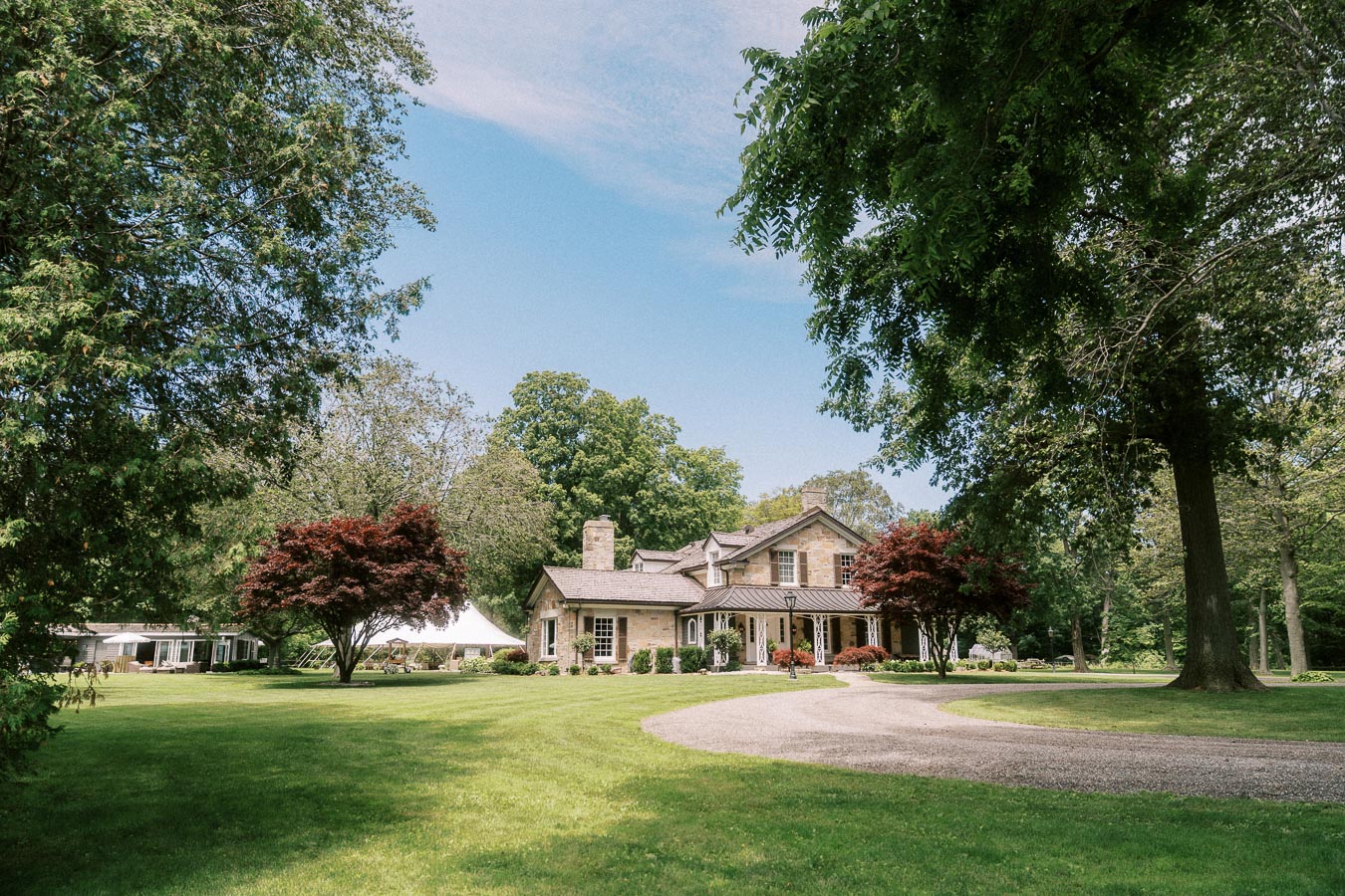 Stone farmhouse on a private Ontario estate with a white wedding tent, gravel driveway, green lawn, gardens, and mature trees.