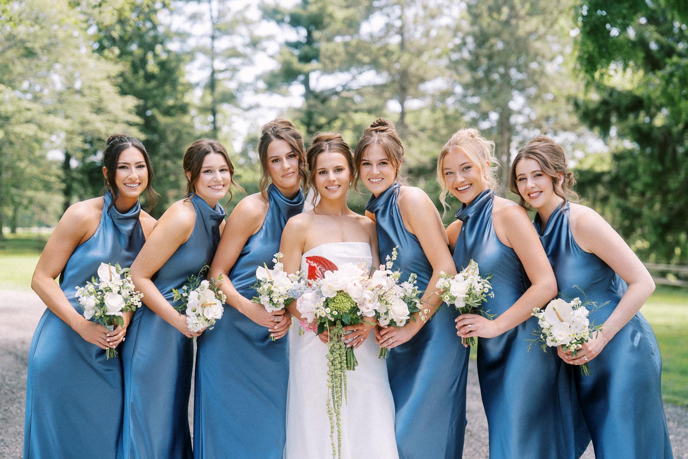 Bride with six bridesmaids in blue dresses holding white bouquets outdoors near Chatham-Kent, Ontario.