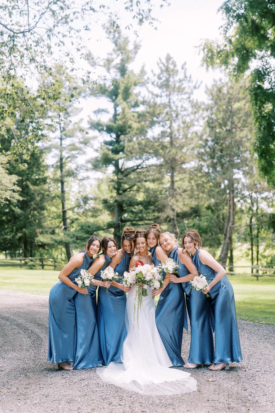 Bride with bridesmaids in blue dresses holding bouquets on a private estate driveway near Chatham-Kent, Ontario.