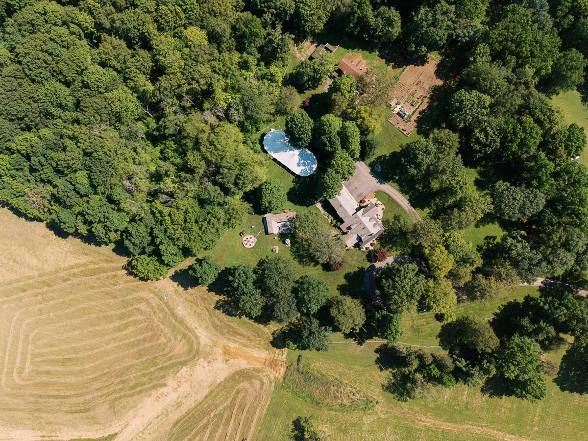 Aerial view of a private estate wedding property near Chatham-Kent, Ontario, with farmhouse, lawns, pool, gardens, fields, and dense trees.