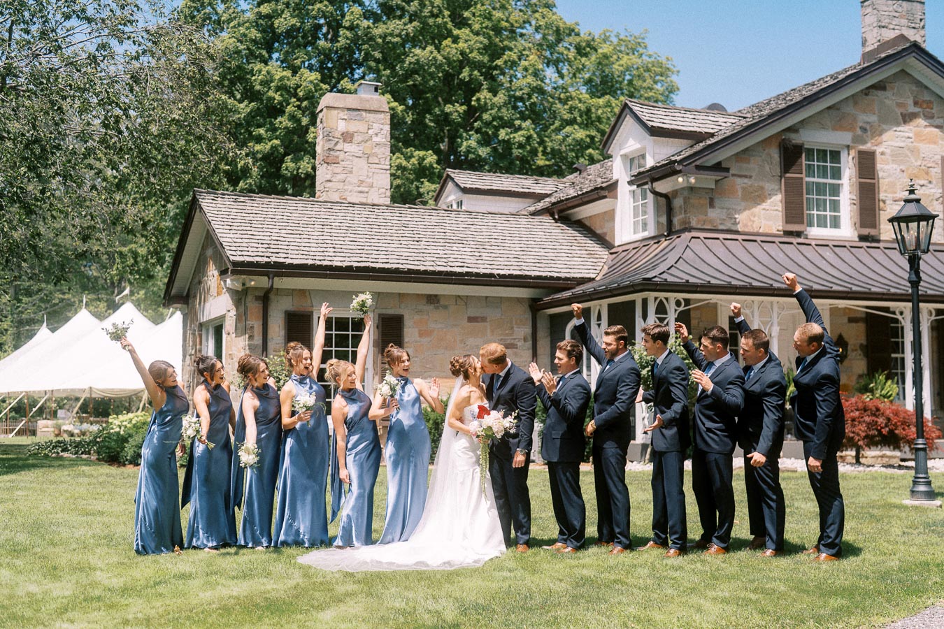Bride, groom, bridesmaids, and groomsmen pose on a lawn beside a stone private estate with a white wedding tent in Chatham-Kent, Ontario.