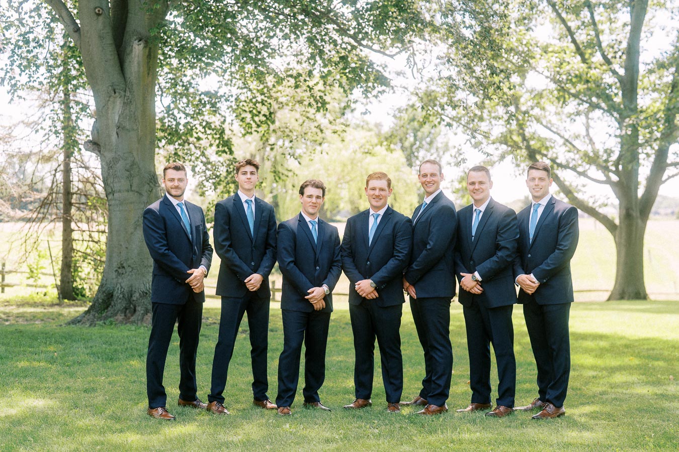 Groom and groomsmen in navy suits standing on a grassy private estate lawn near Chatham-Kent, Ontario, for an outdoor wedding portrait.