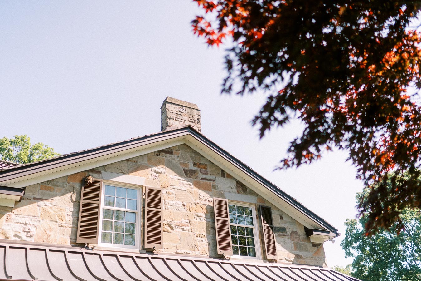 Stone private estate house exterior with shuttered windows, metal roof, chimney, and red maple leaves near Chatham-Kent, Ontario, Canada.