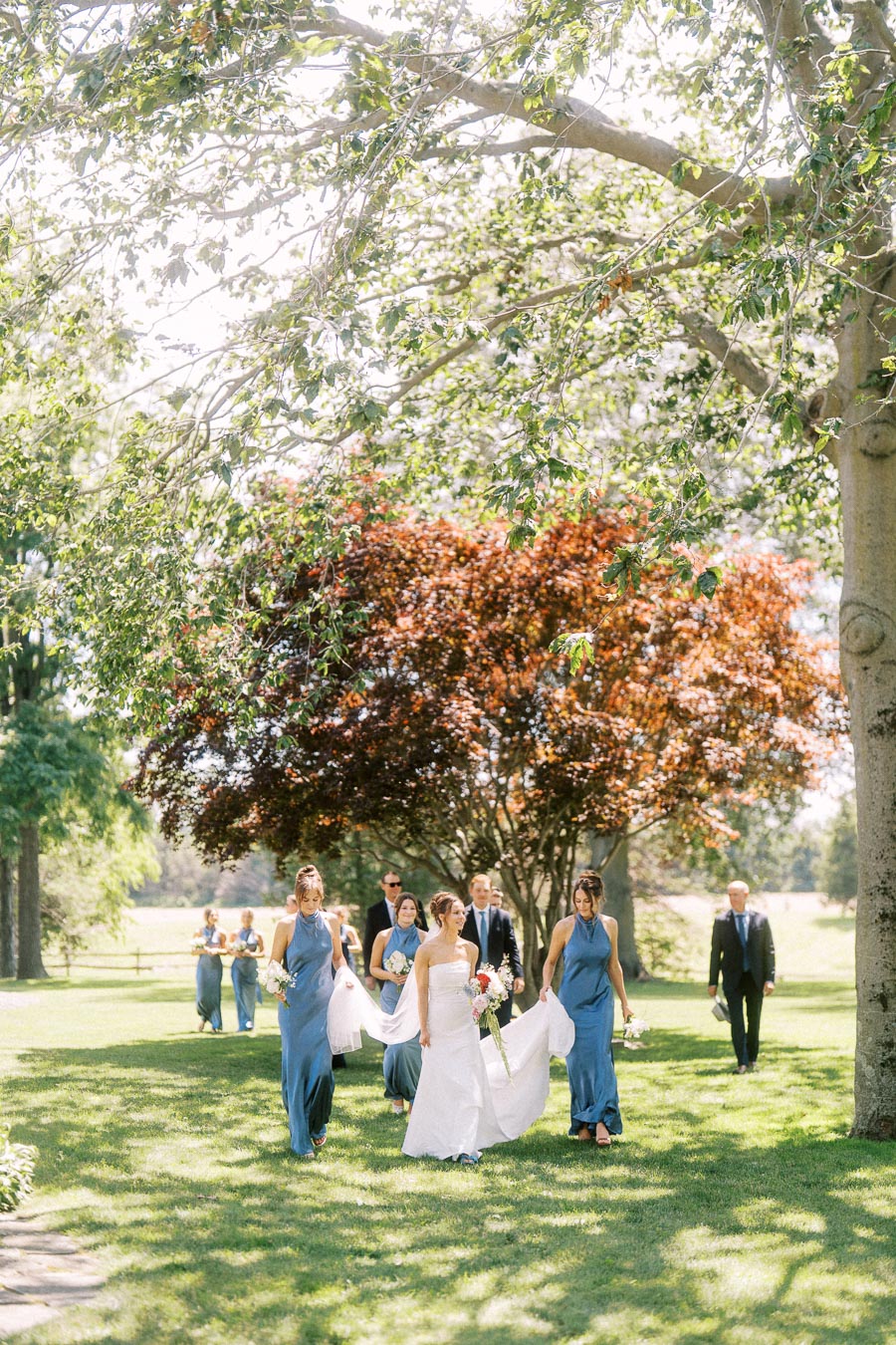 Bride and wedding party walking across a sunlit lawn during an outdoor private estate wedding near Chatham-Kent, Ontario, Canada.