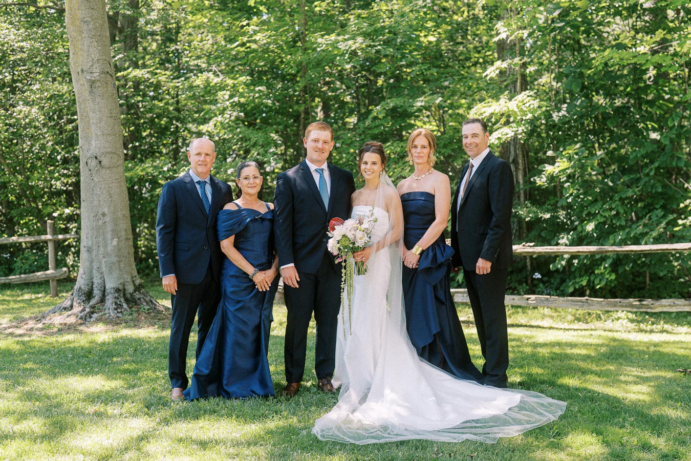 Bride and groom posing with relatives outdoors on a private estate near Chatham-Kent, Ontario, surrounded by trees, grass, and a rustic wooden fence.