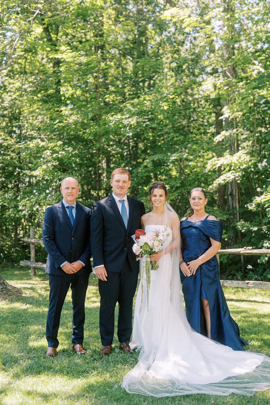 Bride and groom with relatives posing outdoors on a grassy private estate near Chatham-Kent, Ontario, with trees and a rustic fence.
