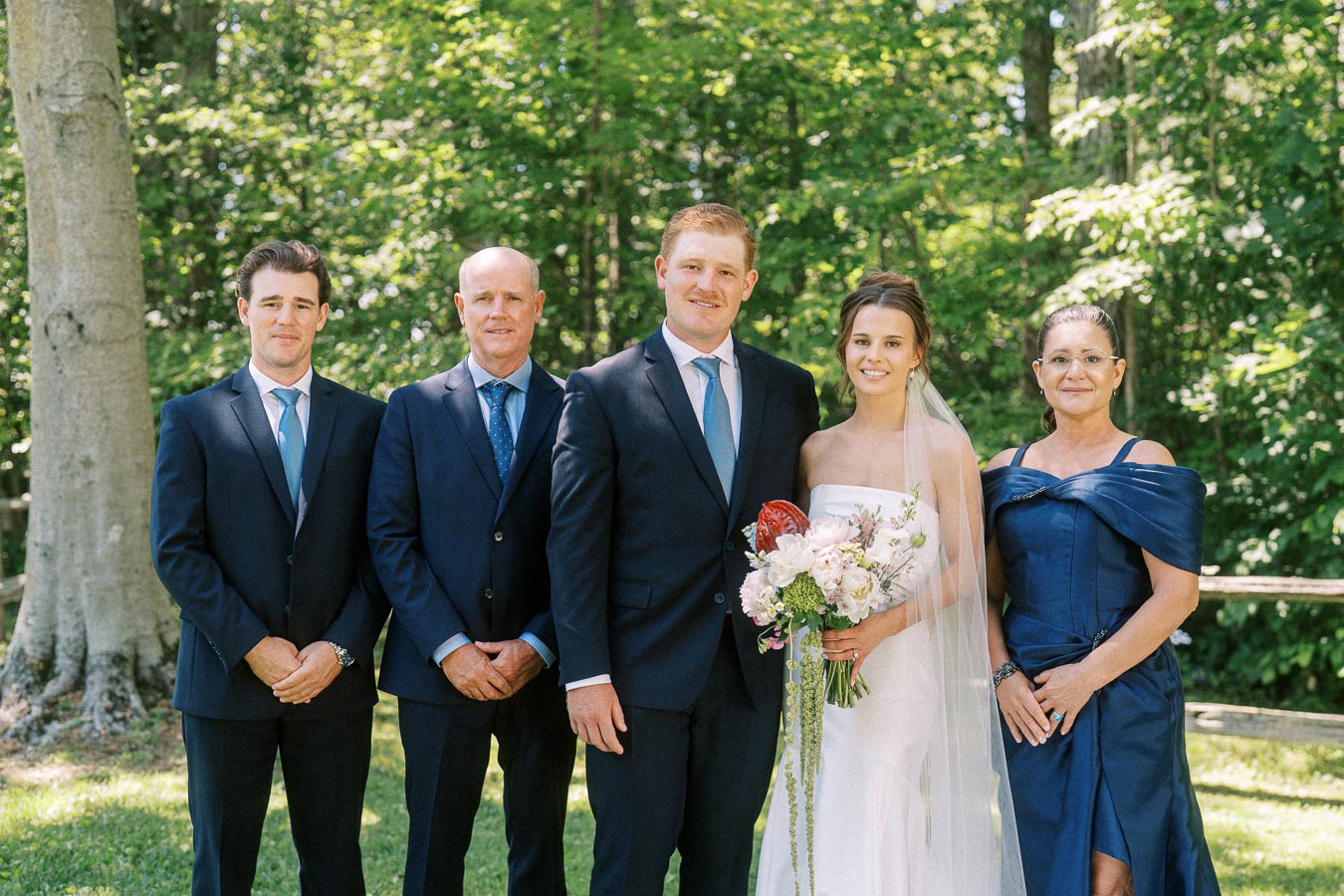 Bride and groom pose with relatives in formal wedding attire outdoors in a wooded private estate setting near Chatham-Kent, Ontario, Canada.