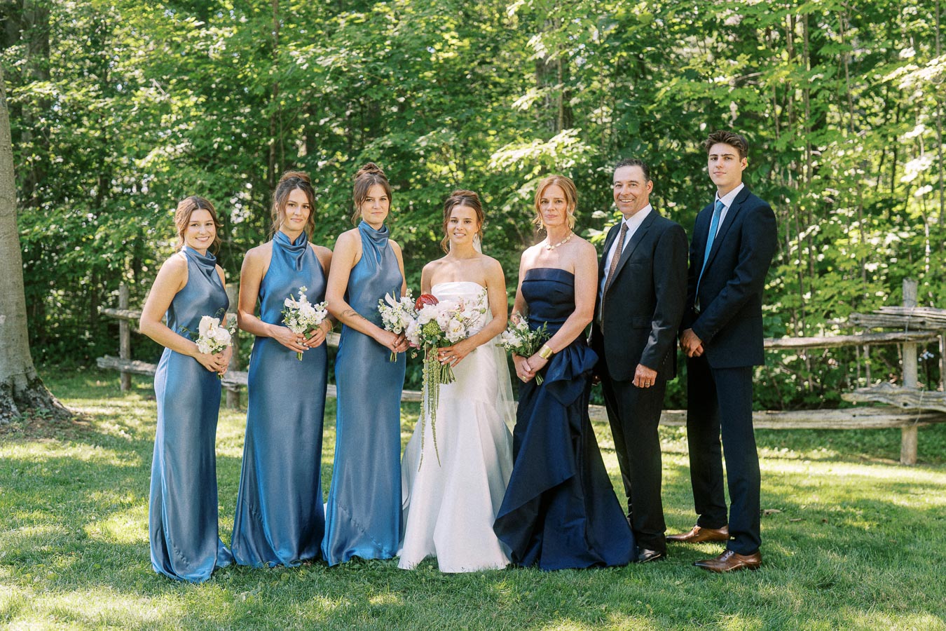 Bride, bridesmaids, and relatives posing for an outdoor wedding portrait on a wooded private property near Chatham-Kent, Ontario, Canada.