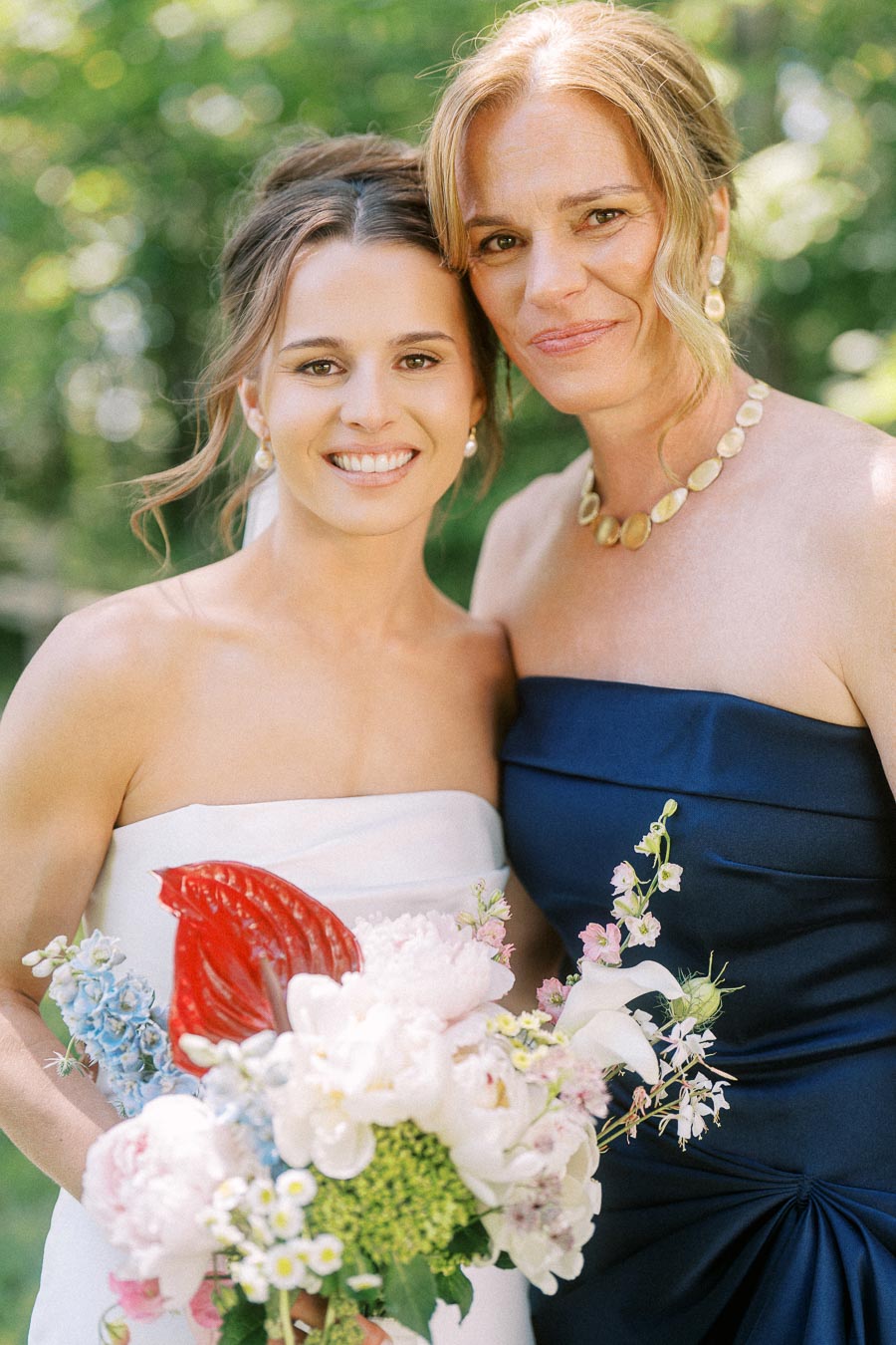 Bride holding a colorful bouquet poses with a woman in a navy strapless dress outdoors near Chatham-Kent, Ontario.
