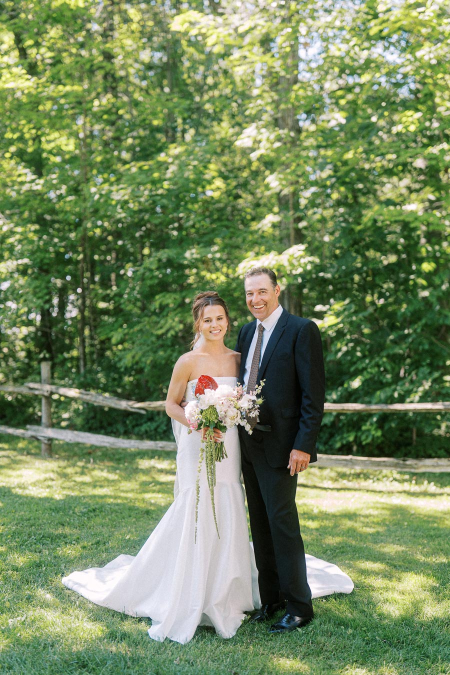 Bride in a white wedding dress holding a bouquet standing with a suited man outdoors on a grassy private estate near Chatham-Kent, Ontario.