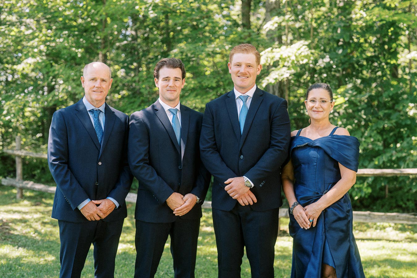 Four wedding guests pose outdoors on a private estate near Chatham-Kent, Ontario, with men in navy suits and a woman in a navy dress.