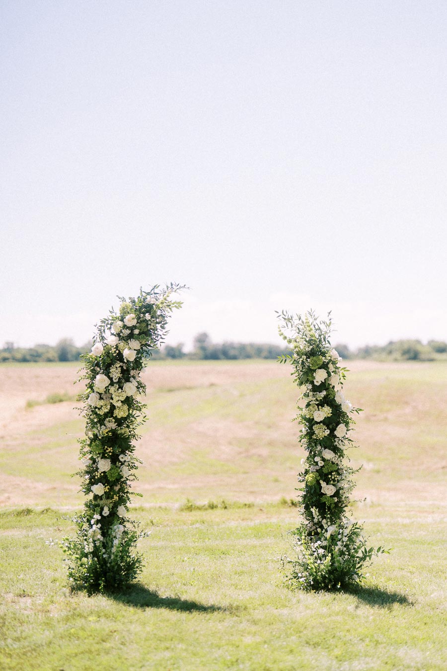 Outdoor wedding ceremony floral pillars with white flowers and greenery on a sunny farm field near Chatham-Kent, Ontario, Canada.