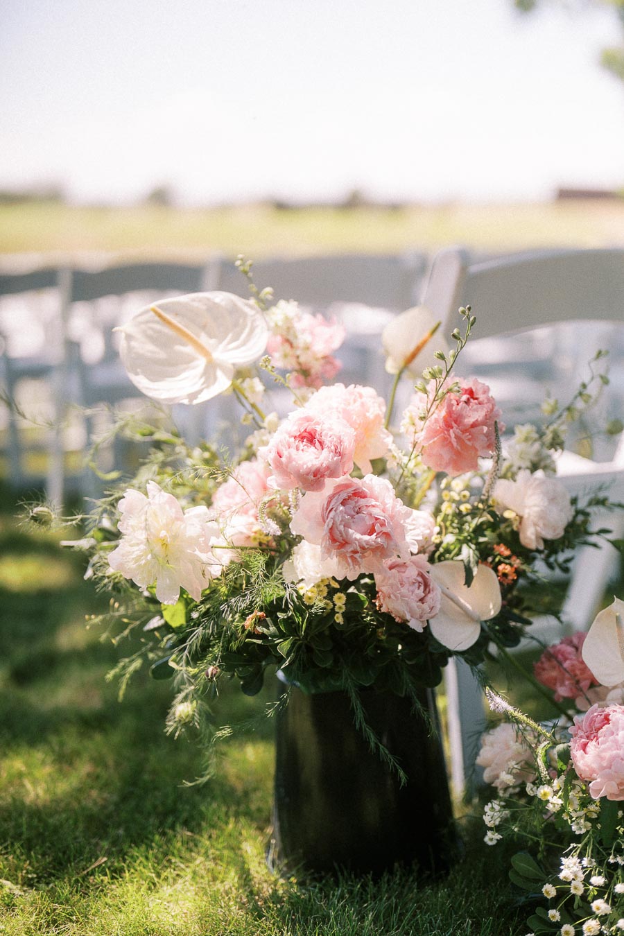 Pink and white floral aisle arrangement beside white chairs at an outdoor wedding ceremony near Chatham-Kent, Ontario.