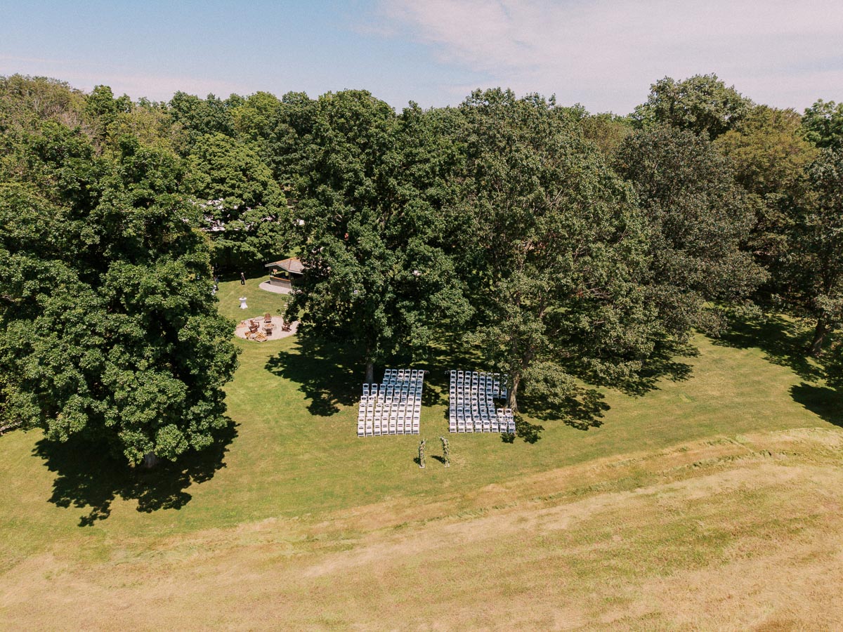 Aerial photo of white chairs set for an outdoor wedding ceremony on a grassy private estate lawn surrounded by trees near Chatham-Kent, Ontario.
