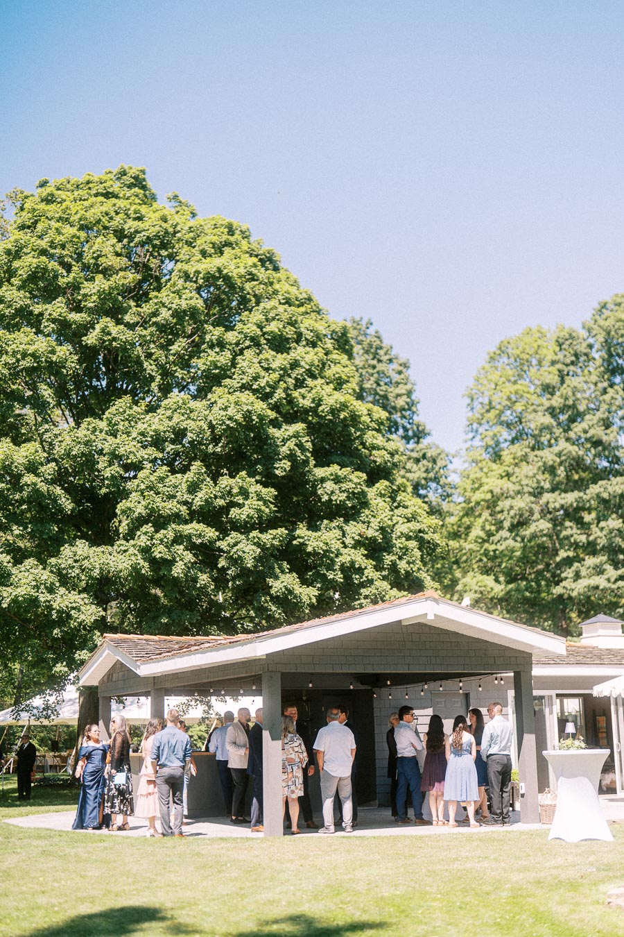 Wedding guests gather for cocktail hour outside a private estate building on a sunny lawn near Chatham-Kent, Ontario, Canada.
