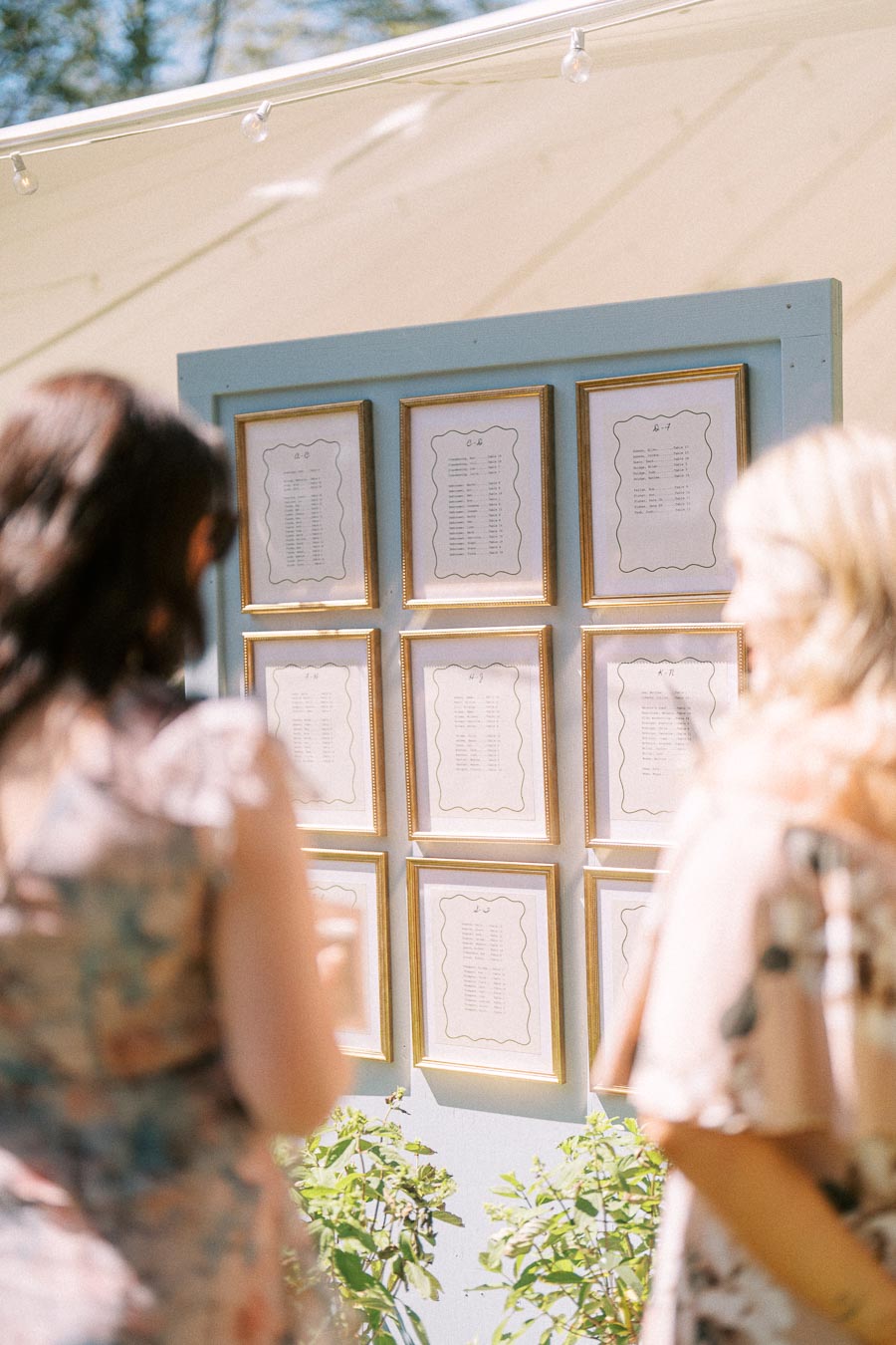Wedding guests look at a framed seating chart display outside a tent during cocktail hour on a sunny private estate near Chatham-Kent, Ontario.