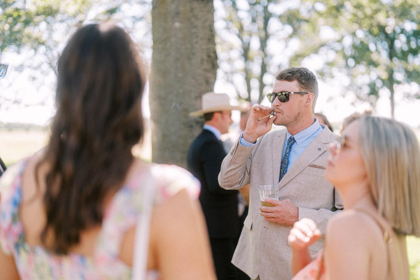 Wedding guests socializing during outdoor cocktail hour on a private estate near Chatham-Kent, Ontario, with a suited man smoking a cigar.
